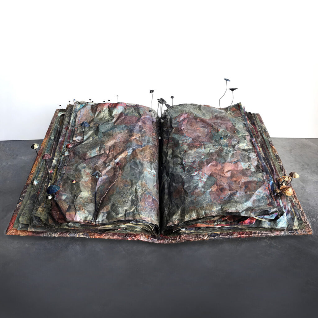 Book of Alchemical Secrets, a patinated copper artist's book shown open with copper mushrooms sprouting out from between its rippled pages
