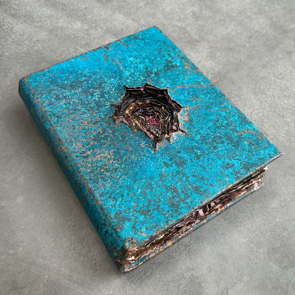 Dangerous Knowledge, a turquoise patinated copper book with a deep wound torn into the cover revealing layers of multi-coloured copper