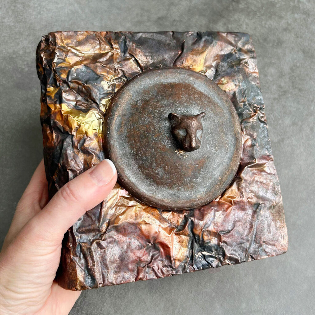 Felines and Other Magical Creatures artist's book held in hand, showing the cast-bronze medallion on the copper cover