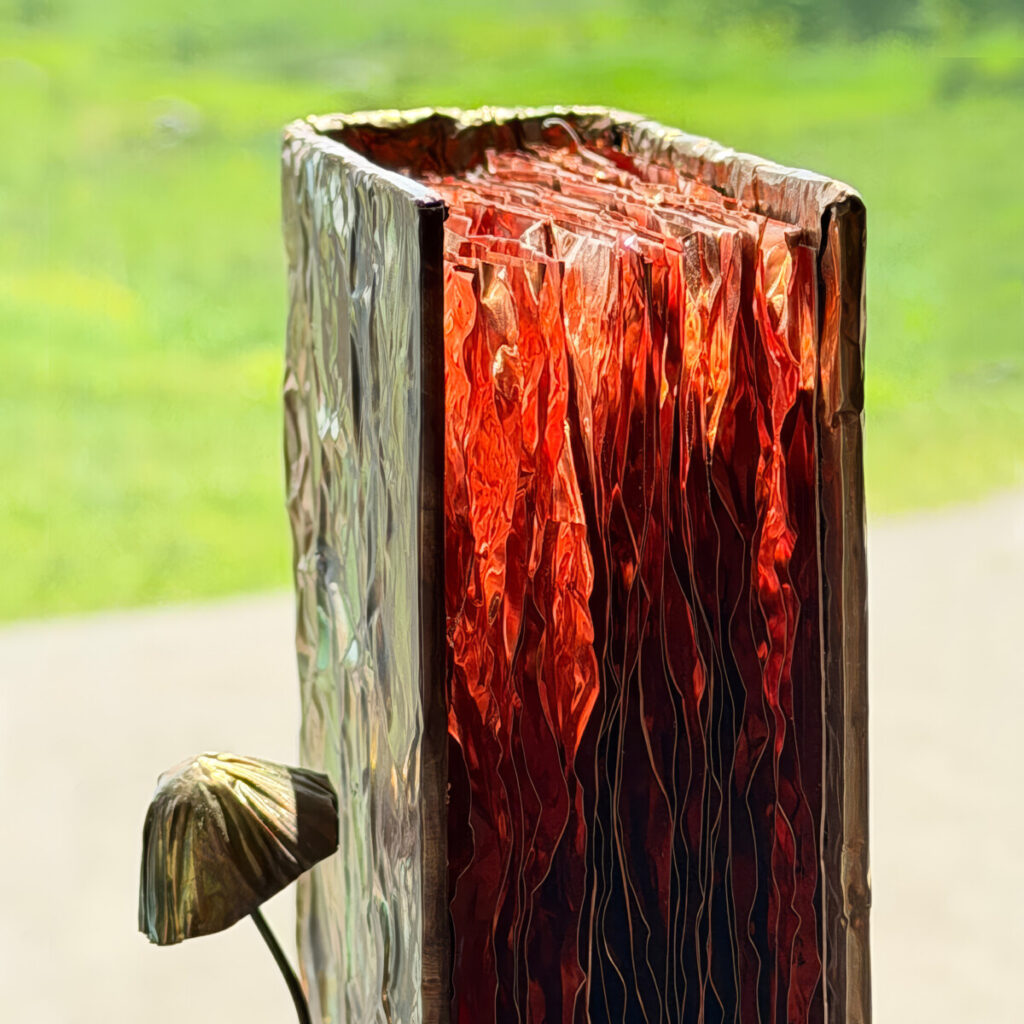 Closeup of Nature Guide for Adventurers standing upright outdoors against a green field, a patinated copper book with a copper mushroom
