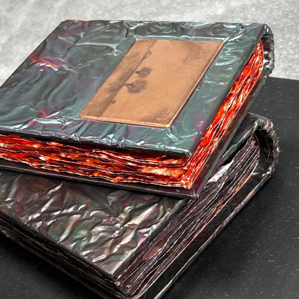 Two Unforgettable Seasons, two stacked patinated copper books at an angle, the top cover set with a Gunnar Norrman drypoint plate