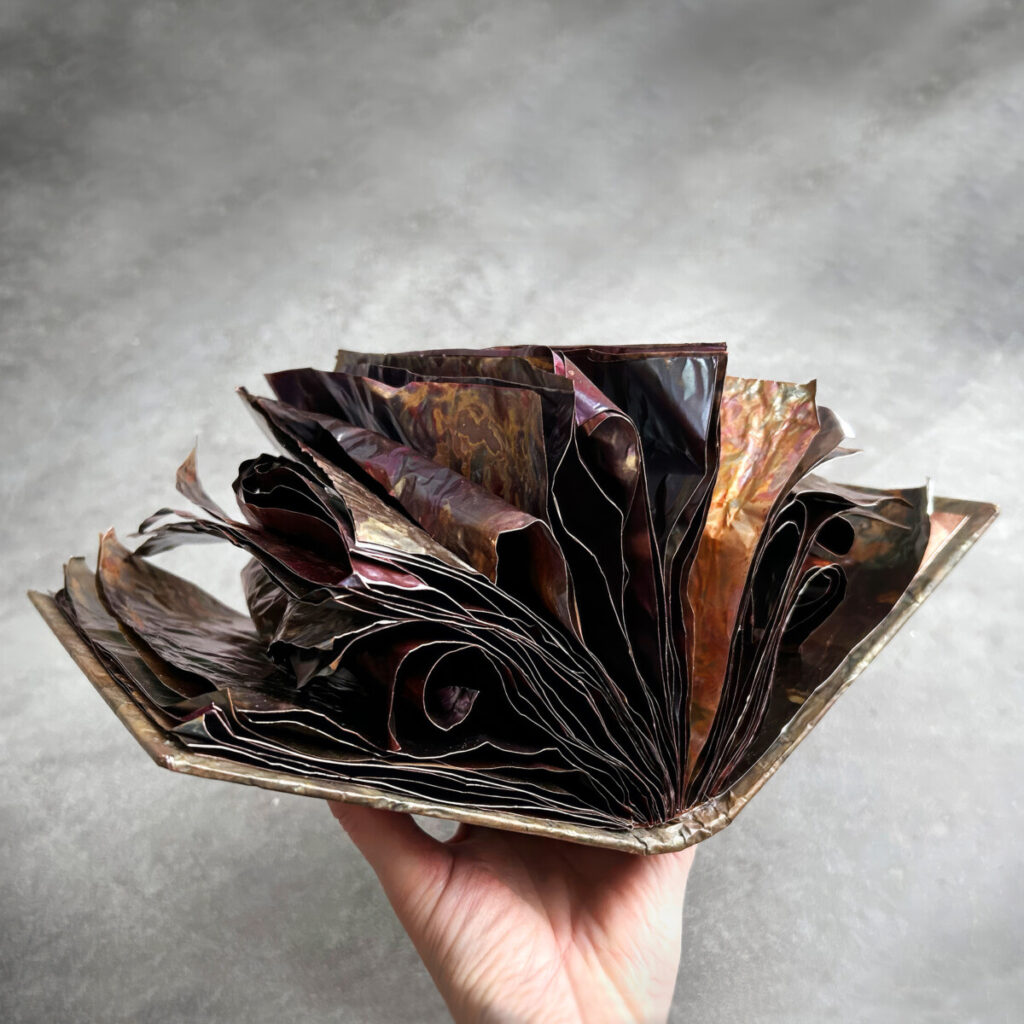 The Unstoppable Story held in hand, open to reveal wild, fanning multi-coloured copper pages
