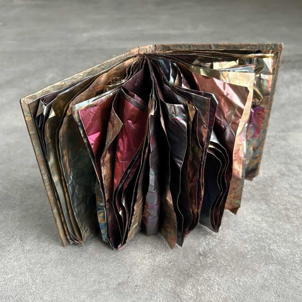 The Unstoppable Story open and standing, its patinated copper pages fanning outward