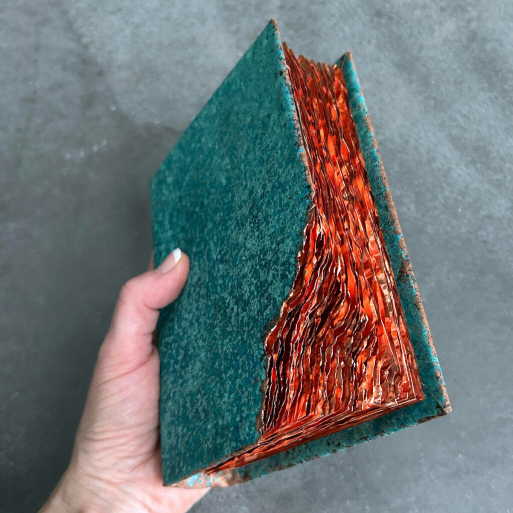 Wilderness Survival Manual held in hand, its turquoise cover has a torn corner showing bare rippled copper underneath