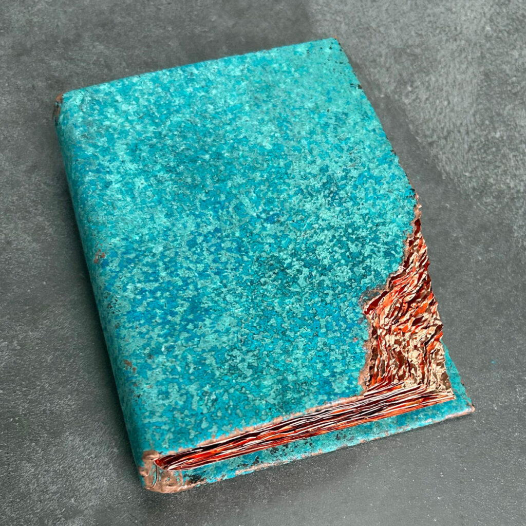 Wilderness Survival Manual, artist's book with a turquoise patinated copper cover and glowing coppery red pages, shown closed at an angle