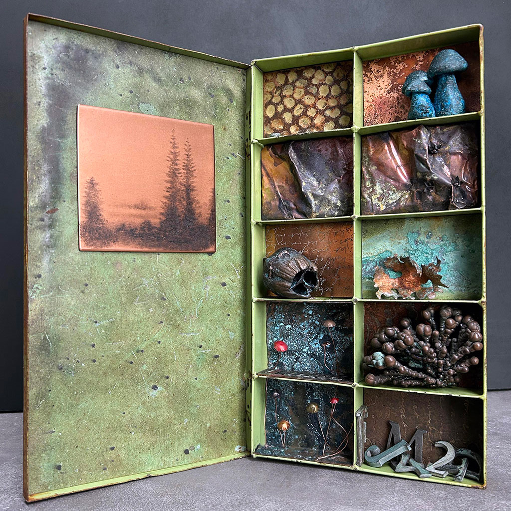 In the Forest Clearing by Marie Louise Kold: an original drypoint plate by Gunnar Norrman mounted on the inside of the lid of an open green metal box, with the small sections on the right hand side filled with patinated copper structures and mushrooms, seedpods and letters, all cast in bronze and patinated.